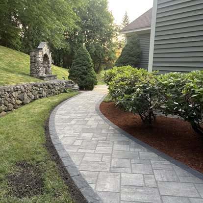 Curved gray paver walkway along a fieldstone wall and fresh mulch beds