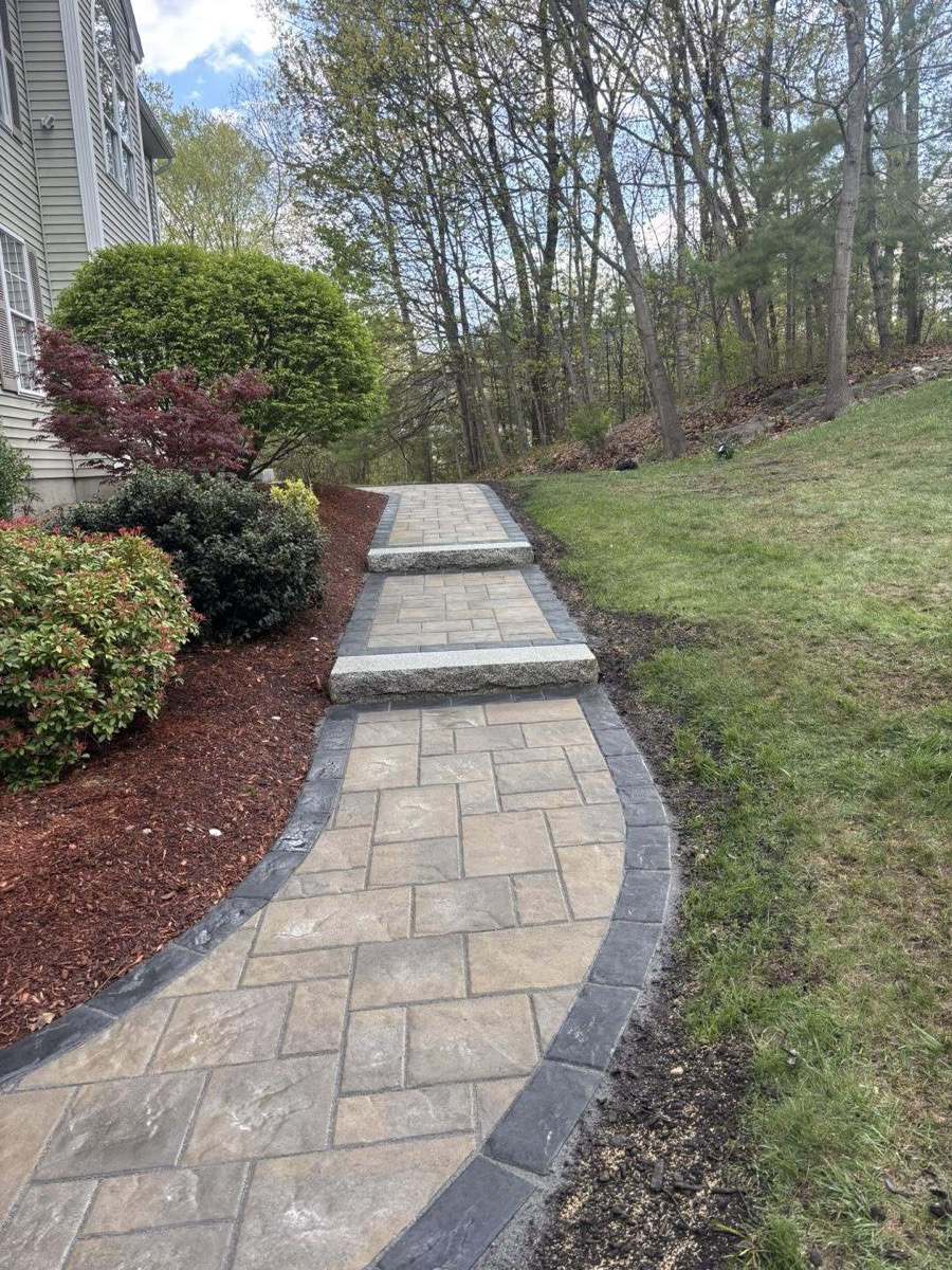 Curved tan paver walkway with stone steps beside mulched planting beds